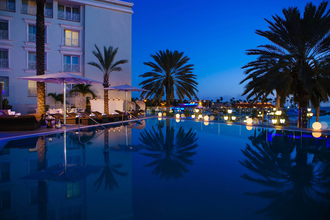 Resort infinity pool at blue hour, lit lanterns and palm reflections