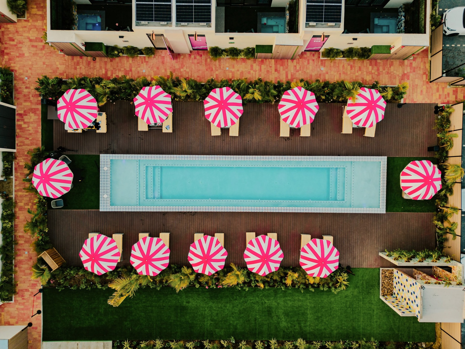 Top-down aerial of the long resort pool framed by pink-striped umbrellas