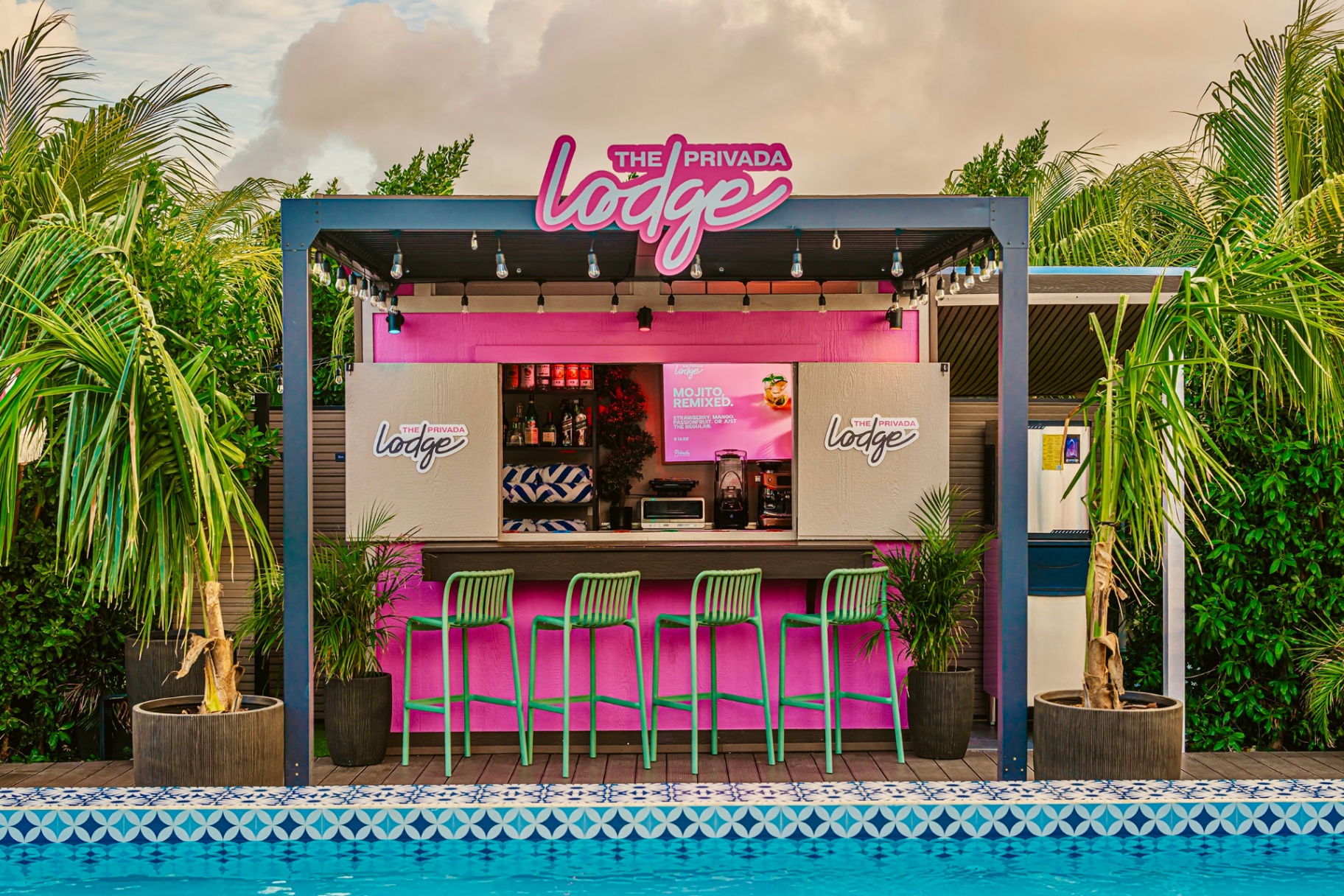 Pink poolside lodge bar with green stools and palms by day