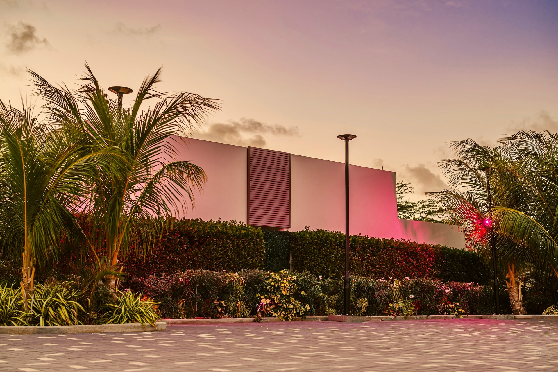 Exterior of Privada Stays at dusk with pink-lit walls and tropical landscaping