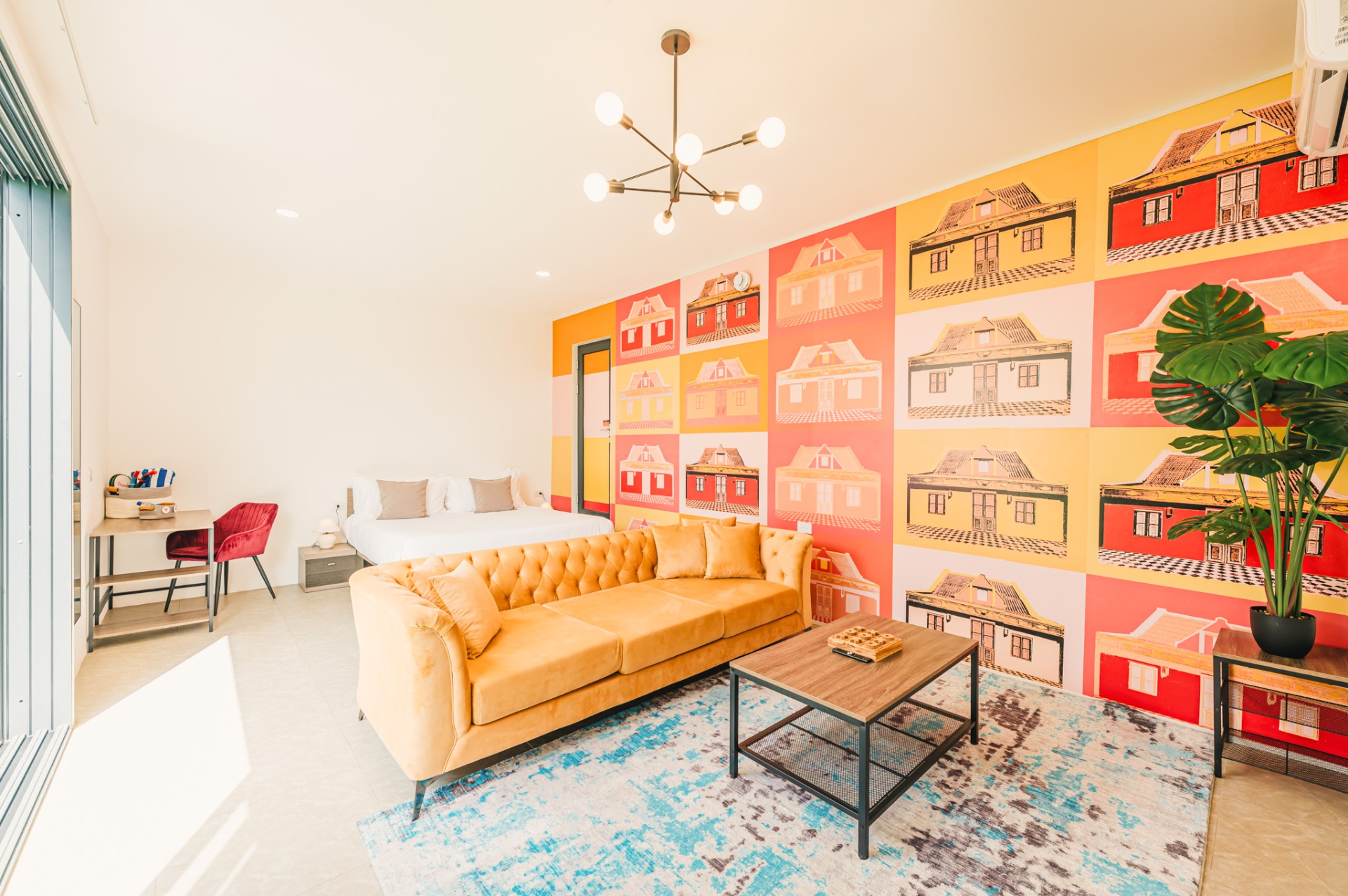 Suite with mustard velvet sofa and pop-art mural of historic Aruban houses