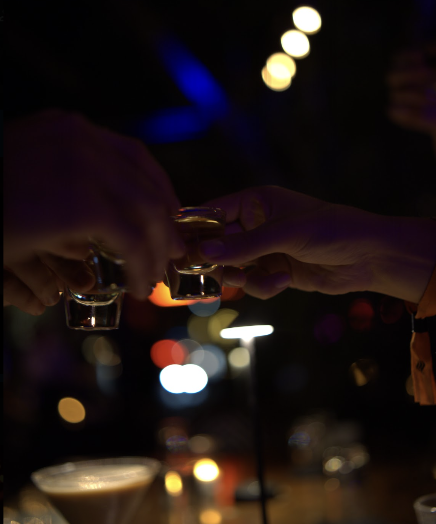 Two guests clink shot glasses across a candlelit bar
