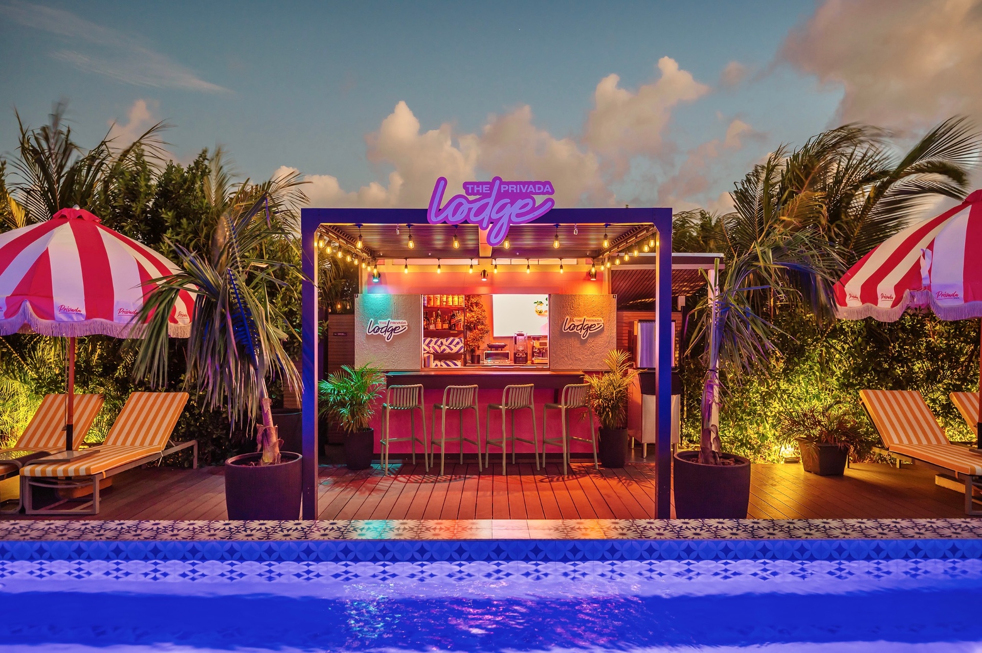 Pink-lit poolside lodge bar at dusk with neon Lodge sign