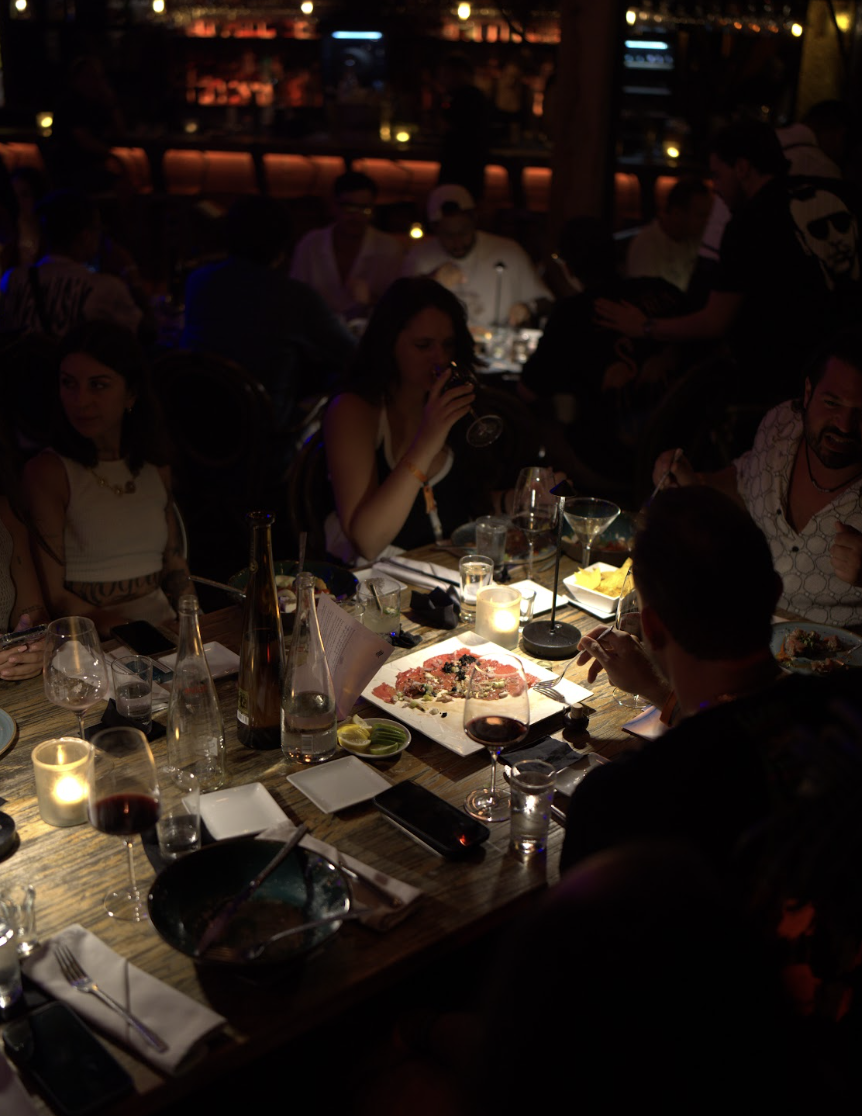 Guests gathered around a long candlelit table over carpaccio and wine