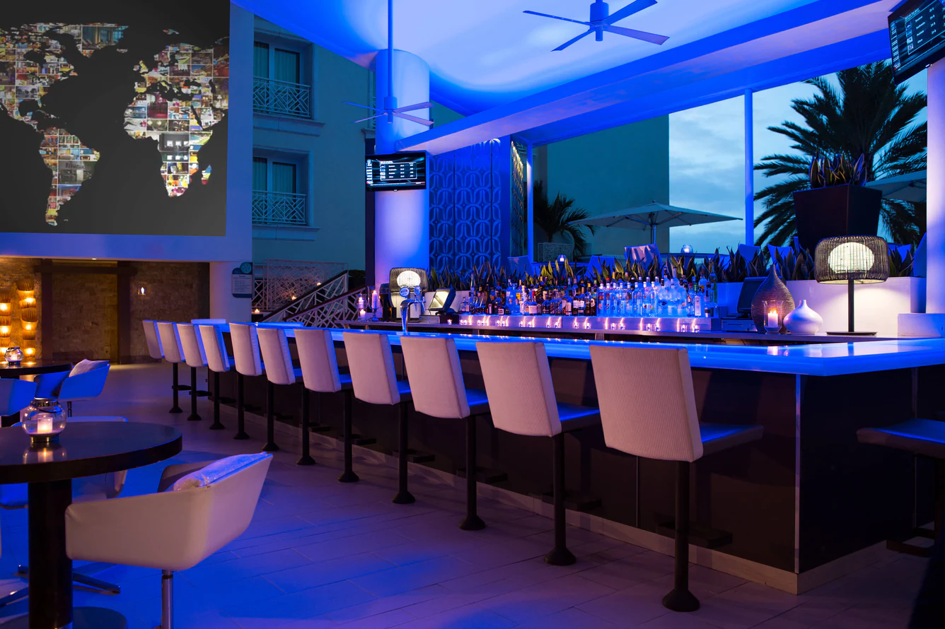 Long lobby bar washed in blue light with rows of bar stools at dusk